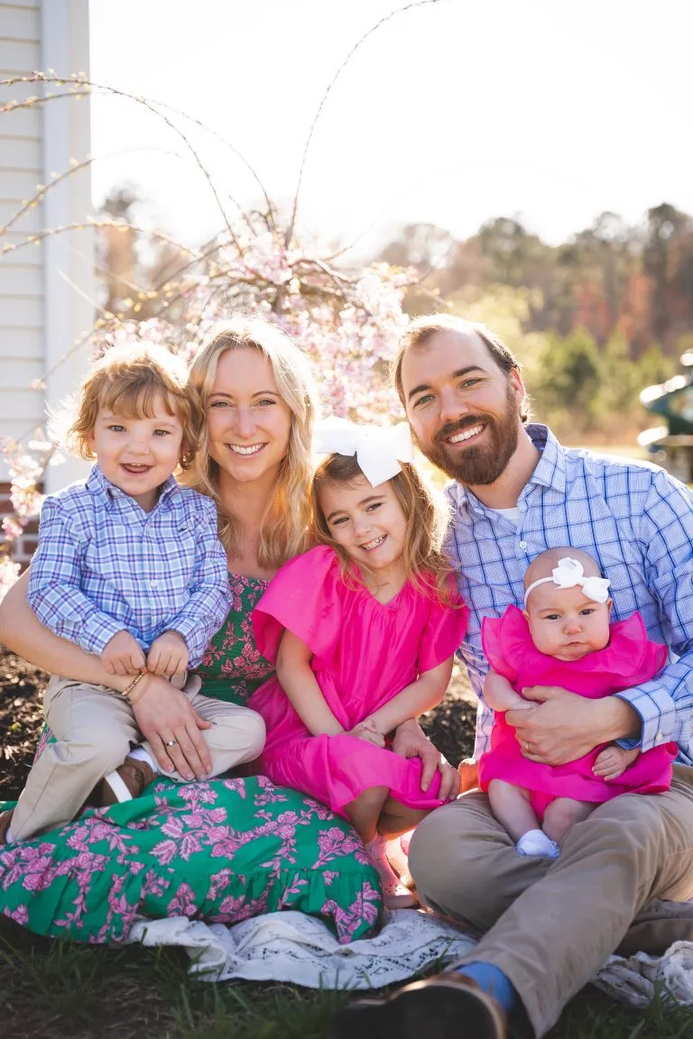 Mallory with her husband Matthew and their three children, smiling outdoors in front of a blossoming tree